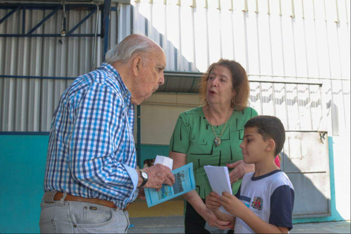 Acompanhado da diretora Conceição, coube ao Marco presentear o visitante ilustre com os desenhos dos colegas